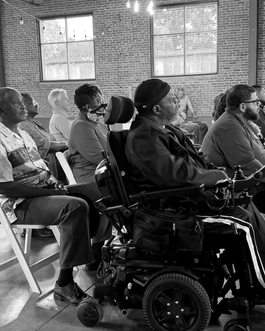 People from across the city seated together and listening, including a man in a power wheelchair