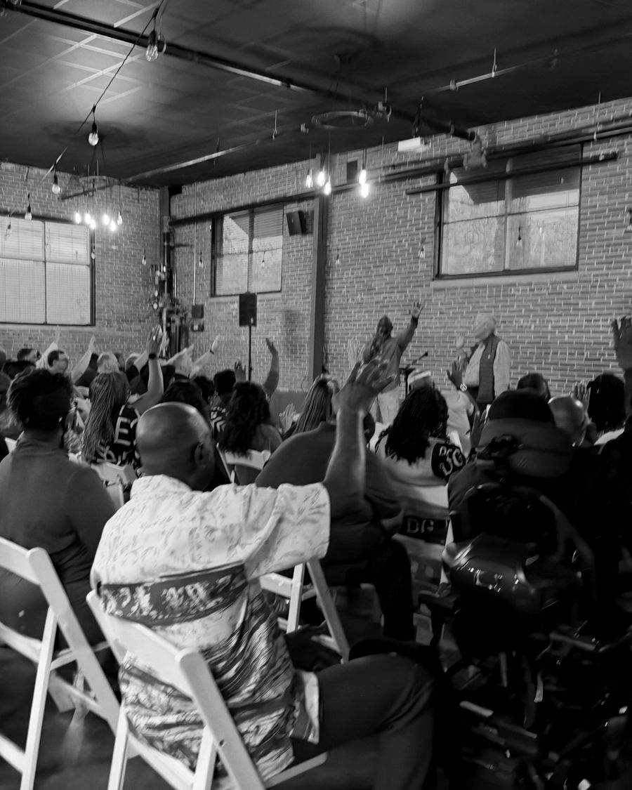 A full room of people raising their hands in worship as leaders lead from the front
